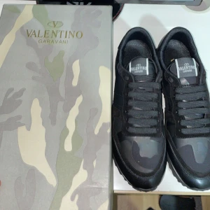 Valentino Garavani sneakers i svart och grått - Snygga Valentino Garavani sneakers i svart och grått med ett coolt camouflage-mönster. Skorna har snörning och en stilren design som passar perfekt för en trendig look. Kvitto följer med boxen