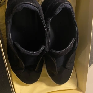 Svarta sneakers från Axel Arigato - Snygga svarta sneakers från Axel Arigato med vit sula. Skorna har en stilren design utan snörning och är perfekta för en minimalistisk look. Märket är diskret präglat på sidan av skorna. De är inte så smutsiga och det går att rengöra och det finns inga repor. Boxen ingår 