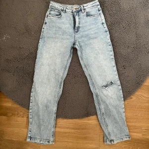 Ljusa jeans med slitning - Säljer ett par ljusa jeans med hög midja och en cool slitning på ena benet. De har en klassisk femficksdesign och stängs med dragkedja och knapp. Perfekta för en avslappnad stil.                        Priset går att diskutera och om du vill ha fler bilder så är det bara att säga till!
