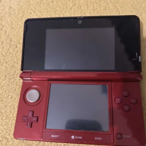 Röd Nintendo 3DS med spel - Säljer en röd Nintendo 3DS med fyra spel: Donkey Kong Country Returns 3D, ett spel för 12 år och äldre, New Super Mario Bros., och Ridge Racer 3D. Perfekt för spelentusiaster som älskar klassiska Nintendo-titlar. Konsolen har dubbla skärmar och är bärbar för spel på språng. priset är väldigt flexibelt villig att diskutera priset 