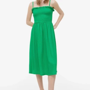Grön klänning med smala axelband - Snygg grön klänning med smala axelband och smockad överdel. Perfekt för sommarens varma dagar. Klänningen har en luftig passform och når till knäna.