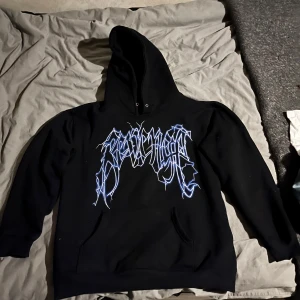 Svart hoodie från Revenge - Säljer en svart hoodie från Revenge med en cool design i blått och vitt. Framsidan har ett grafiskt tryck och baksidan har blixtar. Perfekt för dig som vill sticka ut! (Skriv innan köp)