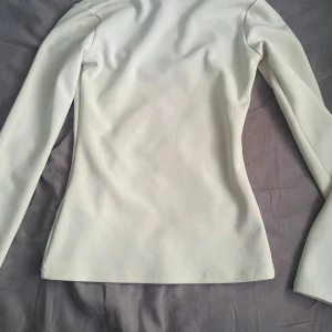 Vit långärmad topp - Säljer en stilren vit långärmad topp med en elegant v-ringad design. Perfekt för att matcha med olika outfits. Toppen har en figurnära passform som framhäver silhuetten.