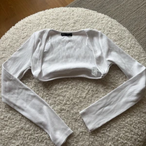 Vit ribbad bolerotopp från Zara - Säljer en stilren vit ribbad bolerotopp från Zara. Perfekt för att lägga till en extra touch till din outfit. Toppen har långa ärmar och är tillverkad i ett mjukt material.