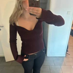 Vinröd ribbad tröja - Säljer en snygg vinröd ribbad tröja med lång ärm och en djup v-ringning. Perfekt för en stilren look. Passar bra till både jeans och kjol.