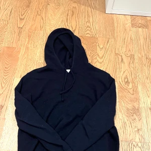 Svart kashmir hoodie från Sayless - Säljer en stilren svart hoodie från Sayless i mjuk kashmir. Perfekt för kyliga dagar med sin bekväma passform och klassiska design. Huvan har dragsko för justering. Ett måste i garderoben för den som älskar komfort och stil.