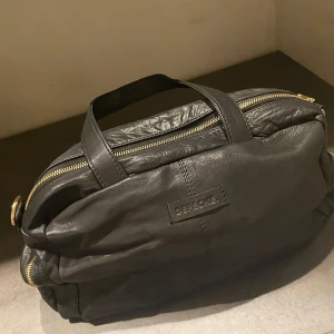 Svart skinnväska från Depeche NWT. - Säljer en helt ny väska från Depeche, Orginal pris 2299kr.svart skinnväska från Depeche med flera dragkedjor och praktiska fack. Perfekt för att hålla ordning på dina saker. Väskan har en stilren design med guldfärgade detaljer och en justerbar axelrem.