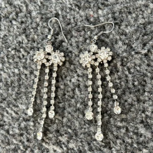 Glittriga silverörhängen med strass - Snygga och eleganta örhängen i silver med glittrande strassdetaljer. De har en hängande design med tre rader av strass som ger en lyxig känsla. Perfekta för att lysa upp vilken outfit som helst.