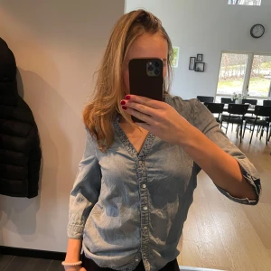 Blå jeansskjorta från Vila - Snygg blå jeansskjorta från Vila med knappar framtill. Skjortan har en klassisk design med långa ärmar och en bekväm passform. Perfekt för en avslappnad stil.