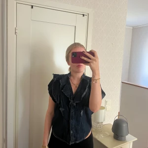 Svart jeansväst med volangdetaljer - Snygg blå jeansblus med volangdetaljer och knappar framtill ifrån Zara! I storlek XS! Knappt använd, köpt via Sellpy!