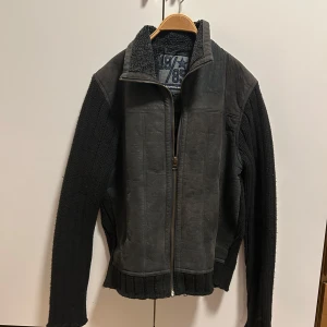 Grå jacka från Scotch & Soda - Säljer en snygg grå jacka från Scotch & Soda med dragkedja och stickade ärmar. Jackan har en mysig fleecekrage och detaljerad design med ett tryck på insidan. Perfekt för kyligare dagar!