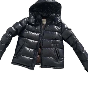 Moncler Maya - Snygg svart pufferjacka från Moncler med glansig finish och dragkedja framtill. Jackan har en huva och långa ärmar, perfekt för kyliga dagar. Storlek 1 = S och är mörkblå. Ett måste för garderoben! Kvitto medföljer. Skriv vid frågor 💬🍾💯