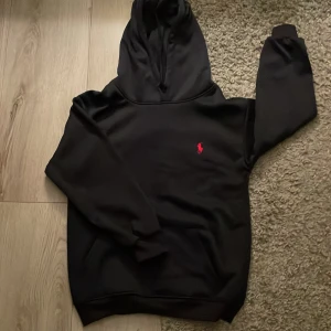 Marinblå hoodie från Ralph Lauren - Säljer en stilren Marinblå hoodie från Ralph Lauren med det ikoniska röda logotypen på bröstet. Tröjan har en klassisk passform med långa ärmar och en praktisk huva. Perfekt för en avslappnad look.