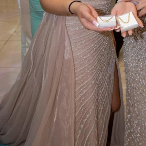 Fest, förlovning, bröllopsklänning  - Elegant champagnefärgad långklänning med glittriga detaljer och en stilfull slits. Säljer denna vackra unika klänning. Perfekt skick kommit till andvändning 1 gång. Storlek 36/S original pris 8000kr pris kan diskuteras vid snabb affär. 