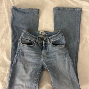 Ljusblå jeansbyxor  - Säljer ett par klassiska ljusblå jeans med fickor och knappgylf. Perfekta för en avslappnad stil. De har en utsvängd passform. Byxorna är i storlek xxs och längd short.
