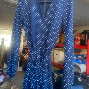 Mörkblå prickig klänning från H&M Divided - Säljer en superfin mörkblå klänning med vita prickar från H&M Divided. Klänningen har en v-ringad design och långa ärmar, perfekt för både vardag och fest. Den har en knytning i midjan som ger en smickrande passform. Materialet känns lätt och bekvämt, perfekt för vår och sommar!