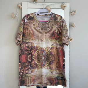 Konstnärlig t-shirt från Eleven Paris x Les (Art)ists - Säljer en unik och konstnärlig t-shirt från  ElevPars och Les (Art)ists. T-shirten har ett detaljerat konstmotiv i flera färger och texten 'JESUS 00' på baksidan. Perfekt för dig som vill sticka ut med en kreativ stil!.vintage storlek L/xl .bred 57cm
