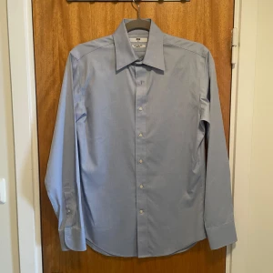 Blå slim fit non-iron skjorta - En blå skjorta från Uniqlo i fint skick, som använts 1-2 ggr innan. Den har slimmad passform, består av 100% bomull och behöver inte strykas efter tvätt. Kombinera gärna med en kavaj till diverse festligheter. Frågor? Skicka ett dm.