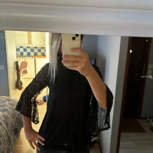 Svart spetsblus med volangärmar - Säljer en snygg svart spetsblus med vackra volangärmar. Blusen har en fin genombruten spetsdesign som ger en lyxig känsla. Perfekt för festliga tillfällen eller en utekväll. Den är i nyskick och har inga frakturer! 