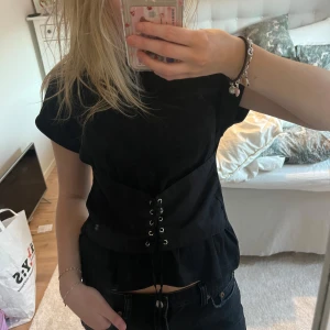 Svart kortärmad topp med snörning - Snygg svart kortärmad topp med snörning framtill. Perfekt för en trendig look. Passar bra till både jeans och kjol.