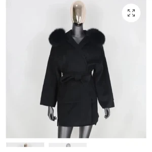 Svart kappa med pälsdetaljer - Snygg svart kappa med fluffiga pälsdetaljer på kragen. Den har en omlott-design med knytband i midjan för en elegant look. Perfekt för kyliga dagar när du vill vara både varm och stilren. Storlek xs/s kan även passa en M 