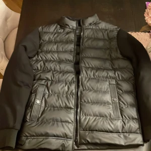 Svart cardigan jacka - Säljer en svart quiltad jacka i mycket bra skick. Den har en dragkedja framtill och är tillverkad i 100% polyester. Jackan är perfekt för höst och vår med sin stilrena design och bekväma passform. Ärmarna är långärmade och jackan har praktiska fickor med knappar. Perfekt för både vardag och lite finare tillfällen!