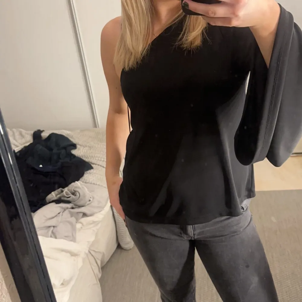 Snygg svart oneshoulder topp från Lindex i storlek M. Perfekt för en utekväll eller fest! Den har en elegant och flytande ärm på ena sidan och är tillverkad i ett mjukt och bekvämt material.. Toppar.