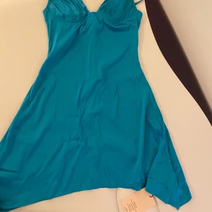  klänning - Snygg blå klänning i ett mjukt och glansigt material. Den har smala axelband och en v-ringad design. Helt ny med prislapp kvar. Passar en XS/S