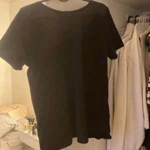 Svart t-shirt från NA-KD - Säljer en svart t-shirt från NA-KD i bra skick. Den har en djup rygg och korta ärmar, perfekt för en avslappnad look. Materialet känns mjukt och bekvämt, vilket gör den idealisk för vardagsbruk. Passar till det mesta i garderoben!