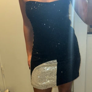 Svart och silver paljettklänning Adoore  - Trendig axelbandslös klänning i svart och silver med glittriga paljetter. Väl använd men i fint skick. Perfekt till fest och nyår! 