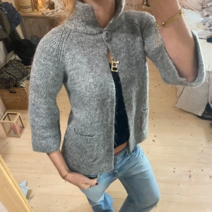 Grå stickad kofta med trekvartsärm - Säljer en mysig grå stickad kofta med trekvartsärm och hög krage. Koftan har en knappdetalj vid halsen och två fickor framtill. Super snygg i jättebra kvalitet ❤️❤️🫶🏼