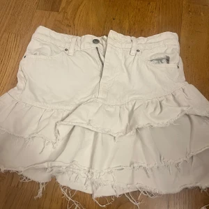 Vit jeanskjol med volanger -  vit jeanskjol med volanger och råa kanter. Kjolen har en dragkedja framtill och bälteshällor. Perfekt för en sommarkväll skriv gärna om de önskas fler bilder 🩷