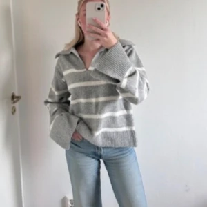 Grå och vit randig tröja - Säljer en mysig grå och vit randig tröja med krage och långa ärmar. Perfekt för kyliga dagar med sin avslappnade passform och ribbade detaljer vid ärmslut och nederkant. Från Gina, även slutsåld !! Nyttskick❤️