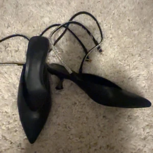 Svarta klackar med spetsig tå - Snygga svarta klackar med spetsig tå och smala remmar runt ankeln. Perfekta för en utekväll eller fest. De har en elegant design som passar till både klänning och byxor.