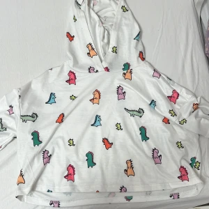 Vit hoodie med dinosauriemönster från Shein - Superfin vit hoodie från Shein med färgglada dinosaurier över hela tyget. Den är perfekt för en chill dag hemma eller en avslappnad utflykt. Hoodien har en skön passform och är gjord i mjukt material. Ett måste för alla dinosaurieälskare! 🦖