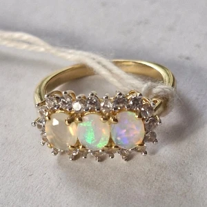 Guldring med opaler och diamanter - Elegant guldring prydd med tre skimrande opaler i mitten, omgivna av gnistrande diamanter. Perfekt för att ge en touch av lyx och stil.                                                                     Ny guldpläterad silver ring med 3 st opaler Stenar: 3 st Etiopiska opaler ca: 0,663 ct och vita zirkoner 20 st ca: 0,600 ct Metall: 925 silver, guldpläterad 1,263 ct Storlek: 50 mm - 15,9