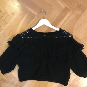 Svart tröja med volangdetaljer - Snygg svart tröja med volangdetaljer och spets vid halsen. Tröjan har trekvartsärmar och en croppad passform, använd fåtal ggr 