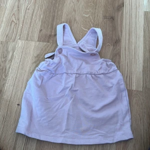 Ljuslila klänning med hängslen från Maxi - Söt ljuslila klänning från Maxi med justerbara hängslen och knappar på sidorna. Perfekt för varma dagar och tillverkad i mjukt bomullsmaterial. Enkel och stilren design som passar till många tillfällen.