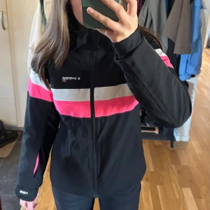 Skidjacka från Everest  - Säljer min snygga gamla skidjacka från Everest med rosa och vita detaljer. Jackan har snöskydd samt en dragkedjsficka på ärmen för liftkort. Den är i bra skick och har en sportig stil med praktiska fickor. Jackan är vattentät, 20 000. Barnstorlek 158, men går att jämföra med en XXS. 