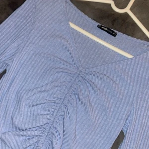 Ljusblå ribbad topp med knyt - Säljer en superfin ljusblå ribbad topp från New yorker . Den har en snygg v-ringning och långa ärmar. Framtill finns en trendig knytning som ger en cool look. Perfekt för både vardag och fest!