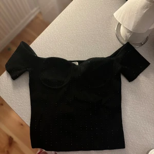 Svart offshoulder topp - Snygg svart offshoulder topp med glittriga detaljer. Perfekt för en kväll ute eller fest. Toppen har en tight passform och korta ärmar som ger en elegant look💗