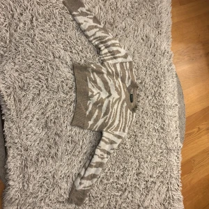 Beige och vit zebramönstrad tröja från SHEIN - Säljer en snygg beige och vit zebramönstrad tröja från SHEIN. Tröjan är croppad med långa ärmar och ribbade muddar. Perfekt för en trendig look!