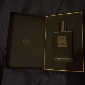 Kilian Smoking Hot - Lyxig parfym i en stilren svart flaska med silverdetaljer. Flaskan ligger i en matchande svart ask med guldkant. Perfekt för den som söker en sofistikerad doftupplevelse.