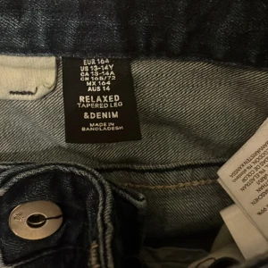 Mörkblå jeans med relaxed tapered fit - Säljer ett par mörkblå jeans från &Denim i storlek EUR 164. De har en relaxed tapered fit som ger en skön och avslappnad stil. Perfekta för både vardag och fest.