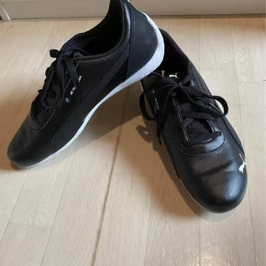 Svarta sneakers från Puma - Säljer ett par svarta Puma BMW sneakers i mycket bra skick. Skorna har en stilren design med vita sulor och klassisk snörning. Perfekta för både vardag och träning. De är bekväma och har en snygg svart färg med vita detaljer. pris kan diskuteras!!