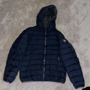 Mörkblå dunjacka från Colmar - Säljer en snygg mörkblå dunjacka från Colmar i mycket bra skick. Jackan har en praktisk huva och dragkedja framtill. Perfekt för kyliga höst- och vinterdagar. Den är quiltad och har långa ärmar för extra värme. Passar både till vardags och lite finare tillfällen. Storlek S, passar även XS