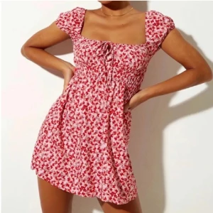 Röd/rosa blommig kortklänning - Superfin röd/rosa kortklänning med blommigt mönster och korta ärmar. Den har en söt knytning framtill och en bekväm passform. Inga skador eller fläckar🌸