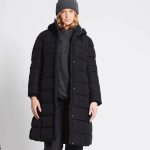 Svart lång dunjacka - Säljer en svart lång dunjacka i mycket bra skick. Den har en mysig huva och stängs med både dragkedja och knappar. Perfekt för kalla vinterdagar! Jackan är långärmad och har en stilren design som passar till det mesta. Håll dig varm och snygg i vinter!