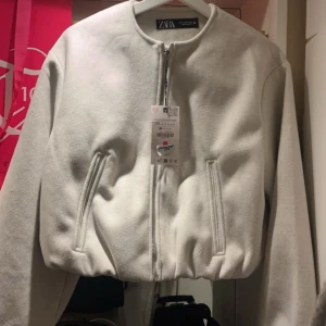 Vit bomberjacka från Zara - Aldrig ansvänd! Säljer en snygg vit bomberjacka från Zara i mycket bra skick den är helt ny med prislappen på. Jackan har en dragkedja framtill och långa ärmar. Perfekt för höst och vår, med en stilren look som passar till det mesta. Storlek Xs.