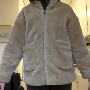 Beige teddyjacka - Mysig beige teddyjacka i mycket bra skick. Perfekt för höst och vinter med sin varma och fluffiga stil. Jackan har långa ärmar och två stora fickor framtill. Den är i en normal passform och känns supergosig att ha på sig. Perfekt för att hålla sig varm och stilren under kyliga dagar!